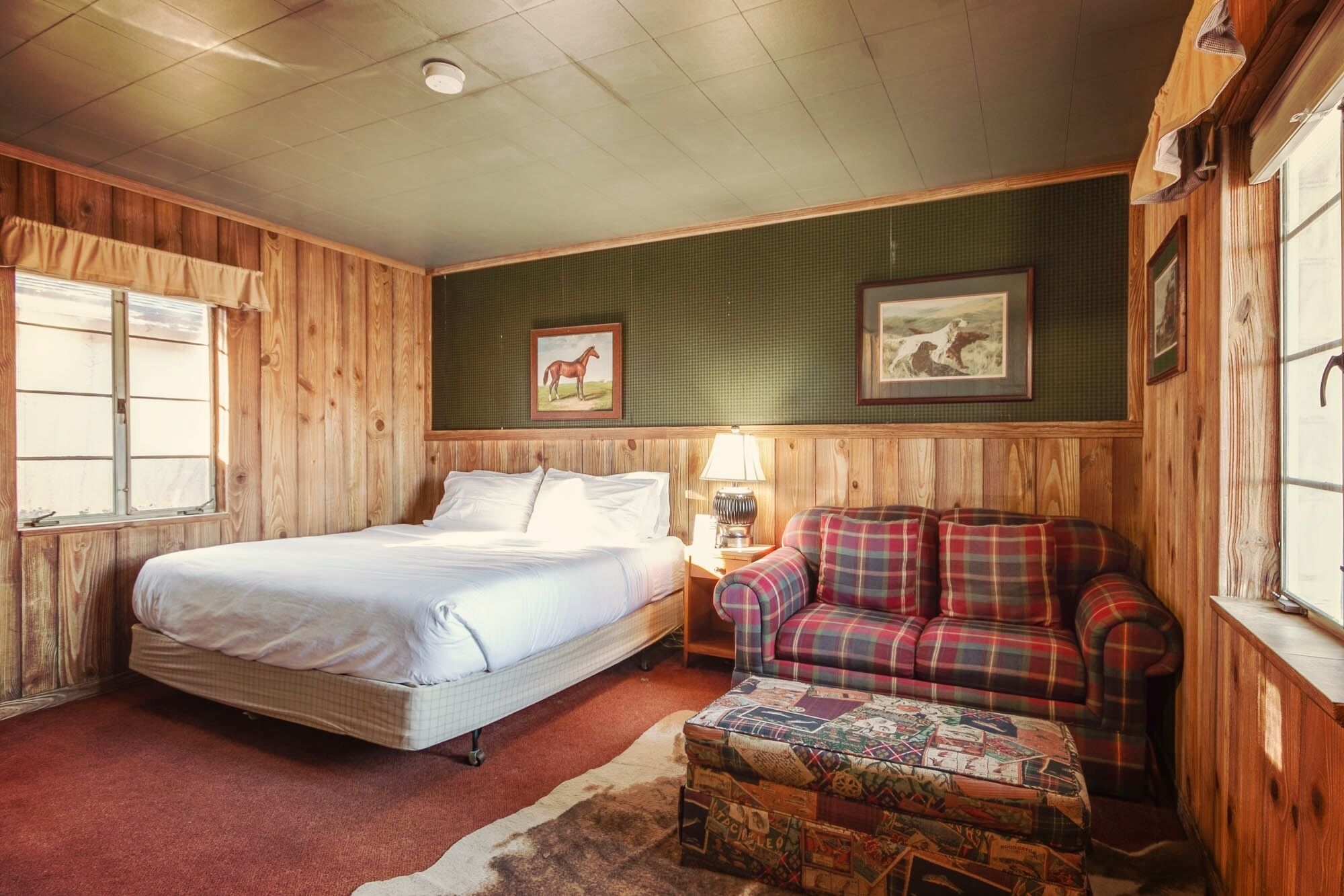 A room with a bed, a plaid sofa, a small table, and two framed pictures on the wall.