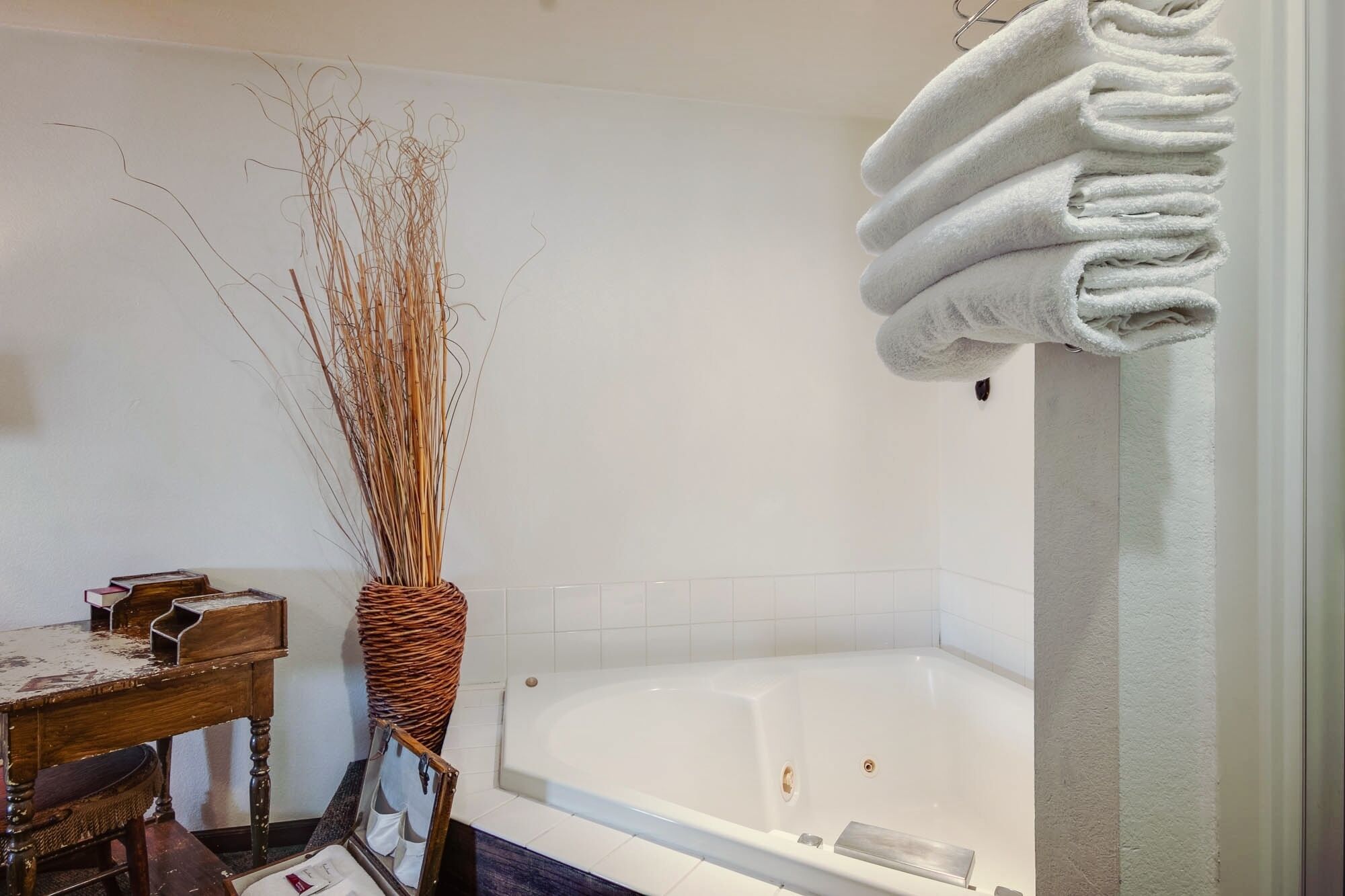 Ein Badezimmer mit einer Badewanne, einem Holzstuhl und einer Korbusvase mit getrockneten Ästen.