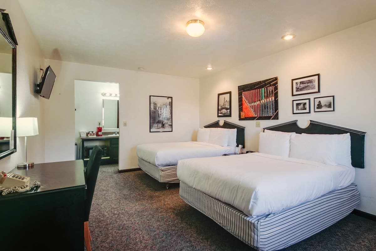 Quarto de hotel com duas camas, uma escrivaninha, um espelho e uma televisão.