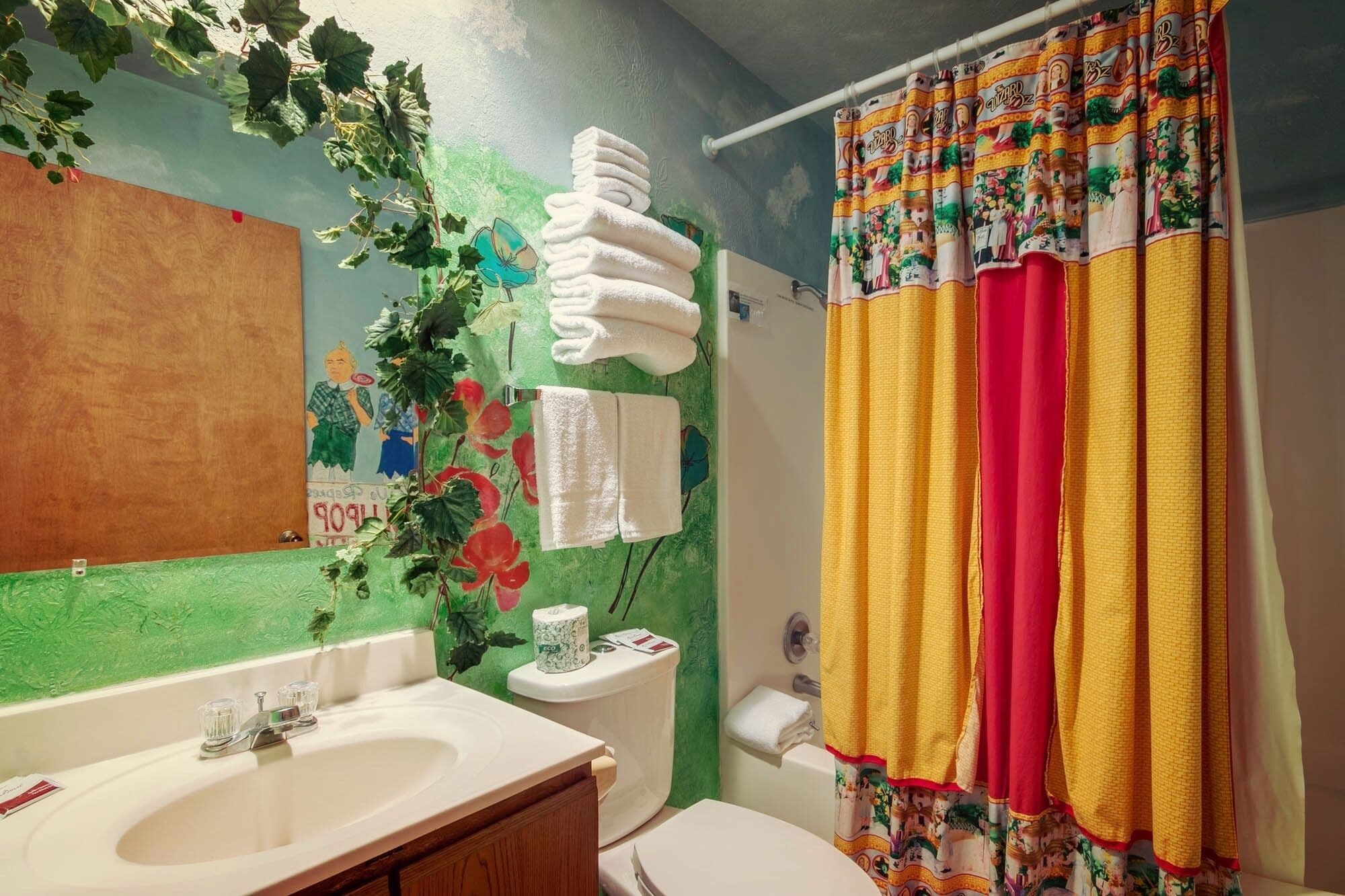 Ein Badezimmer mit grüner Wand, einem Waschbecken, einer Toilette und einem Duschvorhang mit buntem Muster.