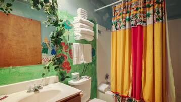 Ein Badezimmer mit grüner Wand, einem Waschbecken, einer Toilette und einem Duschvorhang mit buntem Muster.