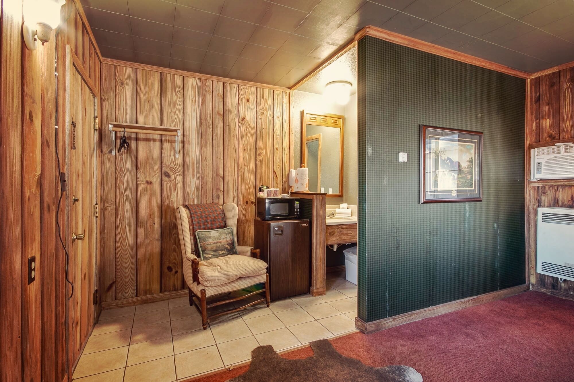 Una habitación con paneles de madera, una silla, un microondas, un lavabo y un cuadro en la pared.