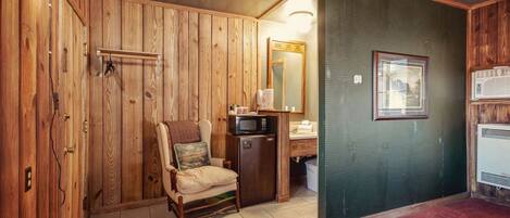 Una habitación con paneles de madera, una silla, un microondas, un lavabo y un cuadro en la pared.