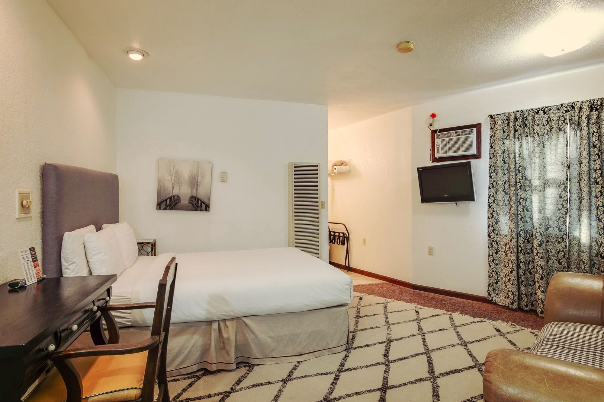 A hotel room with a bed, a desk, a chair, a TV, and a window with curtains.
