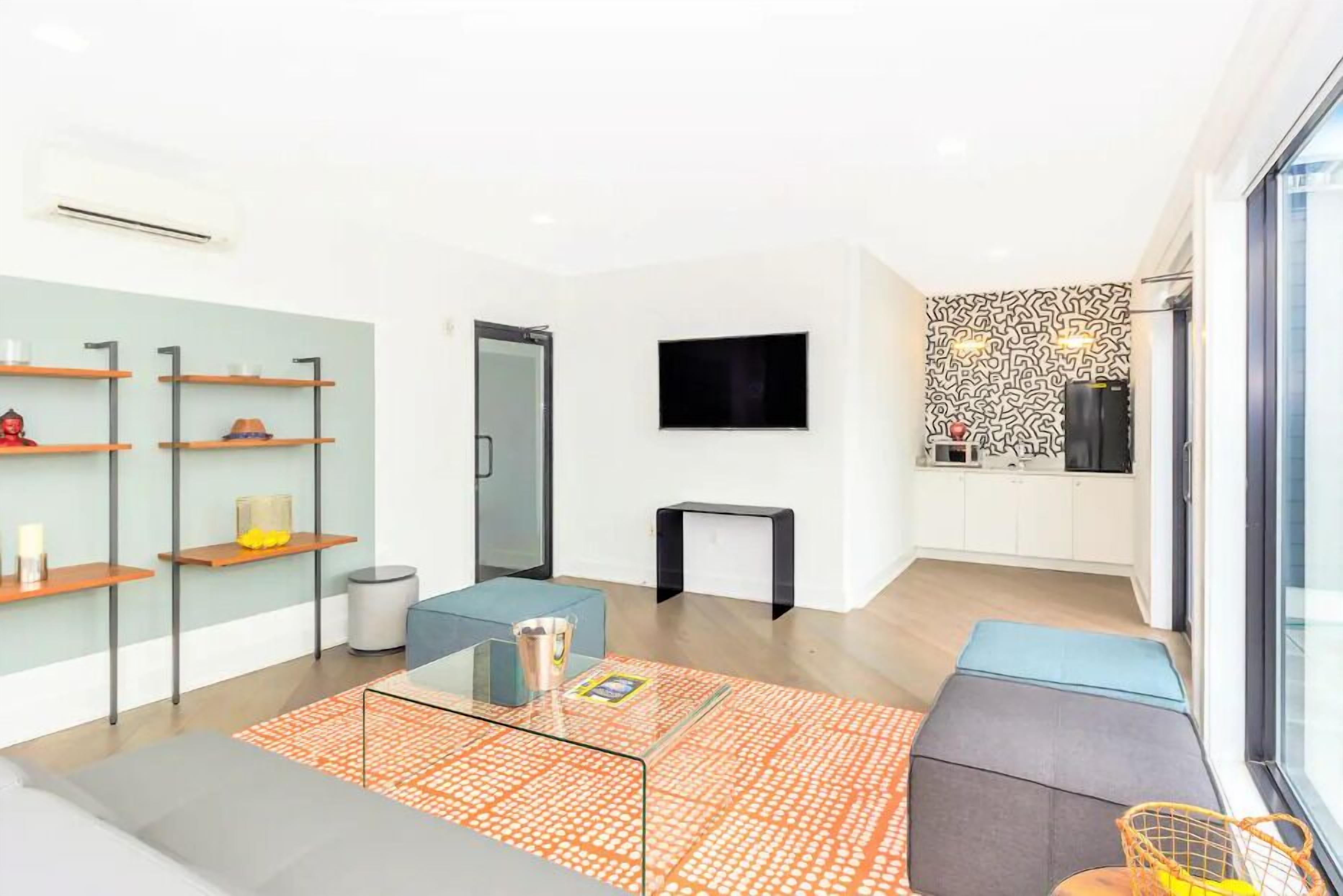 Ein modernes Wohnzimmer mit Sofa, Couchtisch und Regalen. Ein Fernseher ist an der Wand befestigt und im Hintergrund ist eine Wand mit Muster zu sehen.