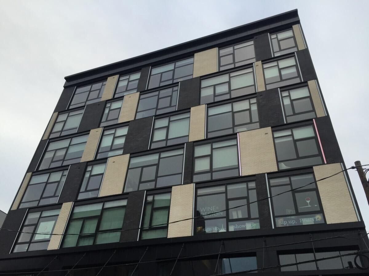 Un edificio de varias plantas con un diseño arquitectónico moderno, que presenta una cuadrícula de ventanas y una combinación de paneles de fachada oscuros y claros.