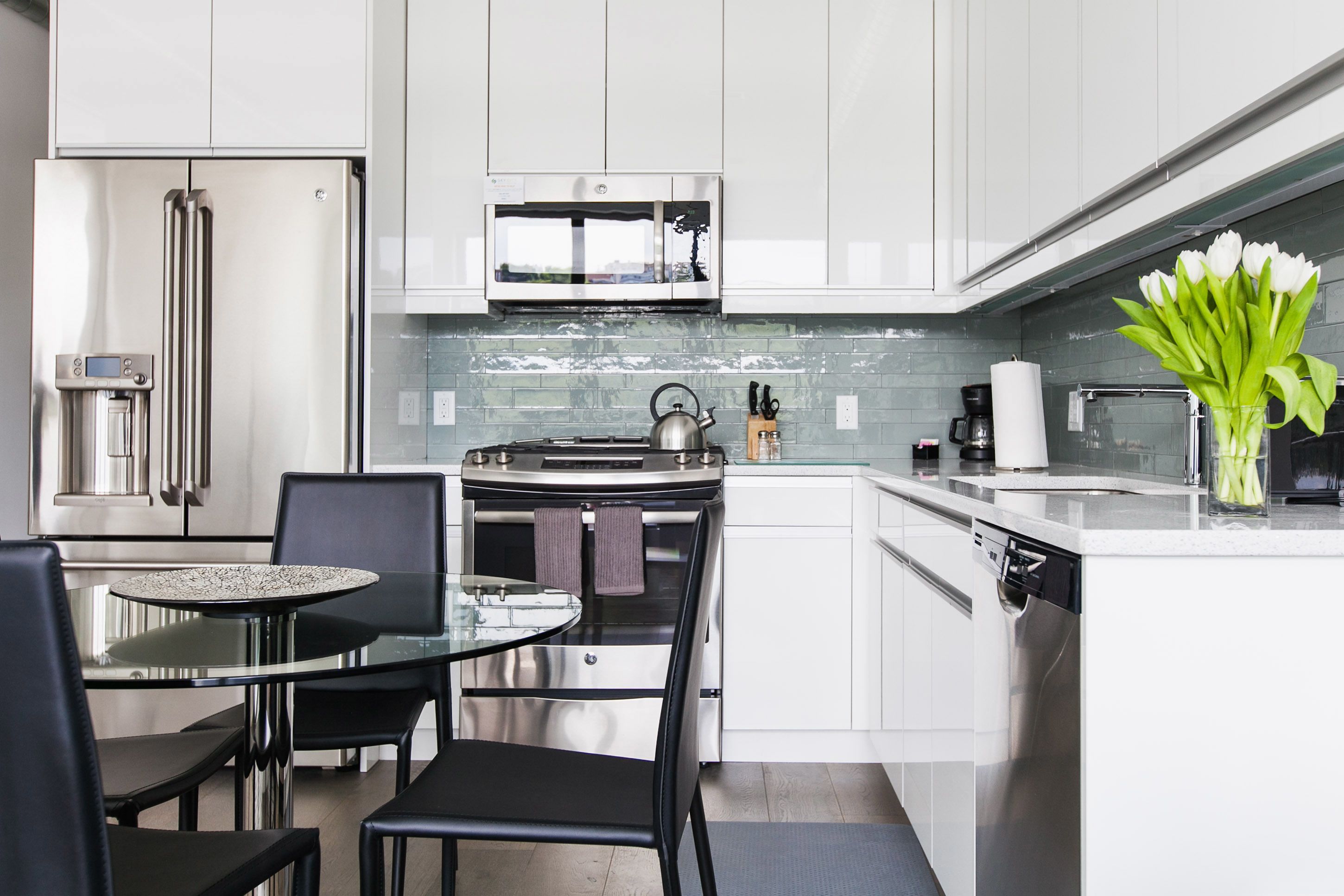 A modern kitchen with stainless steel appliances, a glass dining table, and a vase of flowers.