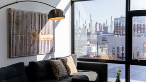 Un salon moderne avec une grande fenêtre, un canapé foncé et une vue sur les toits de la ville.