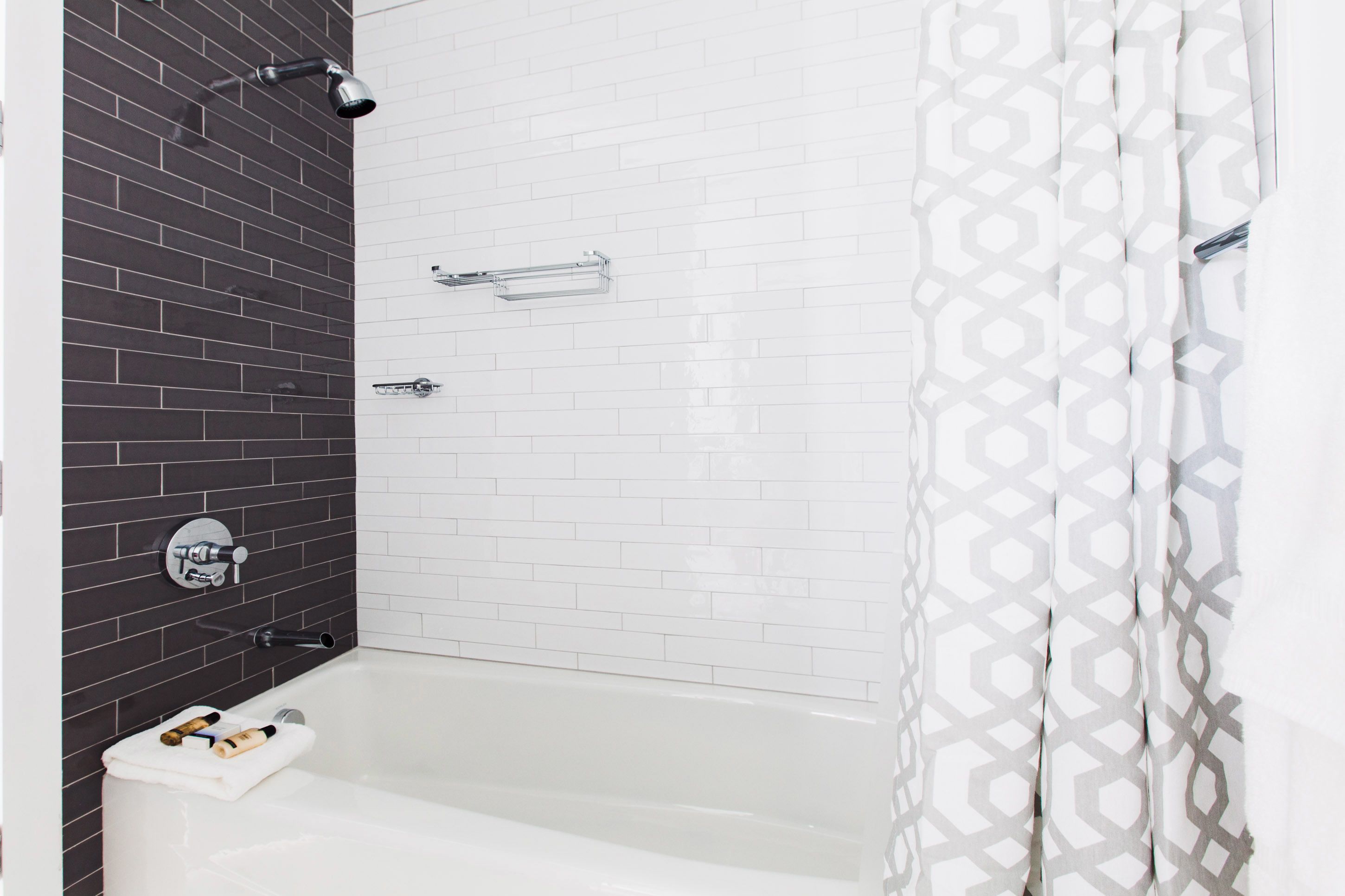 A bathroom with a white bathtub, a shower with a black tiled wall, and a patterned curtain.