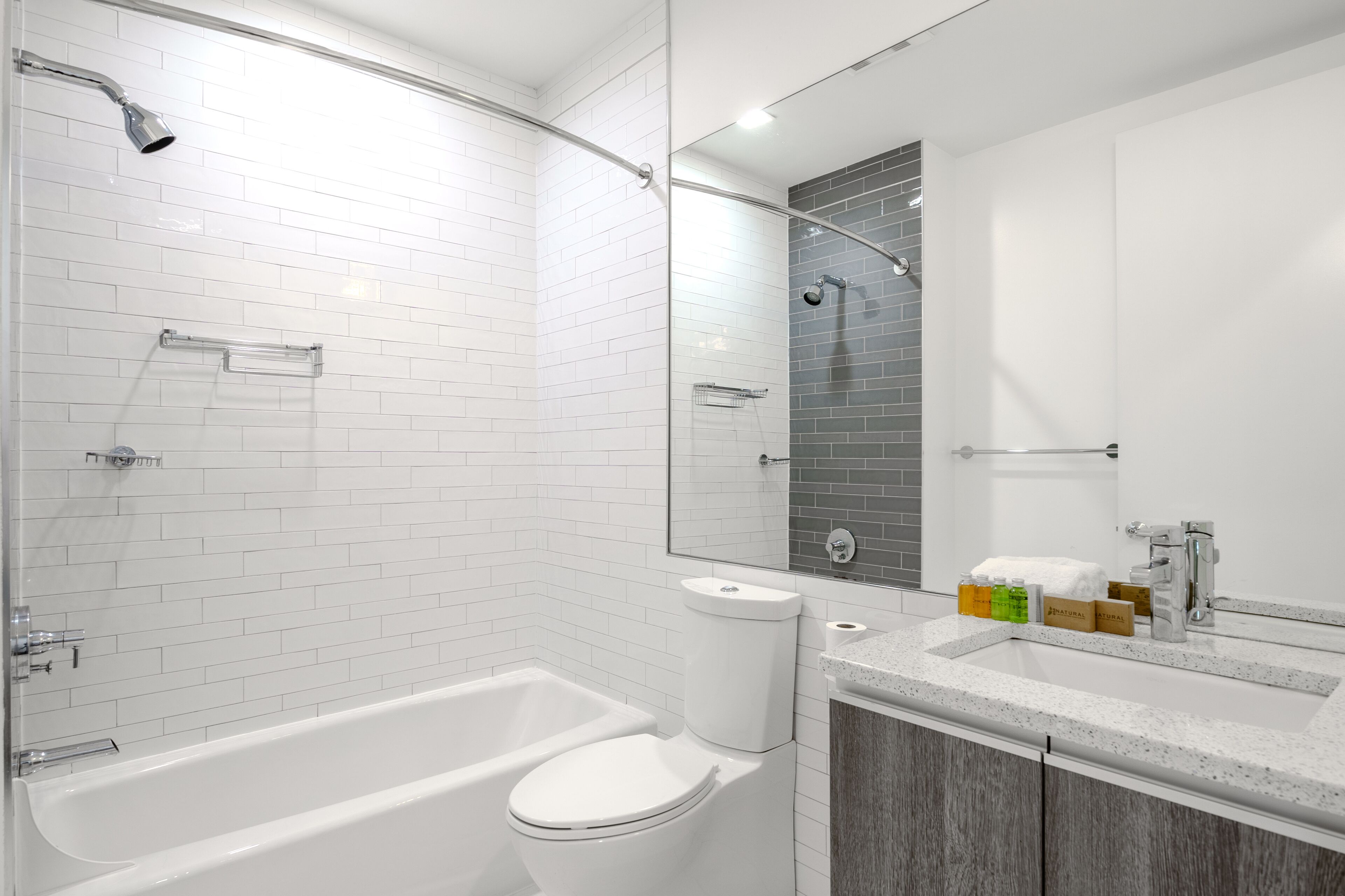 A modern bathroom with a white bathtub, a toilet, and a sink with a mirror above.