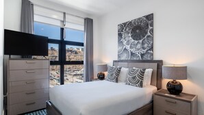 Une chambre d’hôtel moderne dotée d’un grand lit, d’un téléviseur à écran plat, d’une table de chevet avec une lampe et offrant une vue sur la ville par la fenêtre.