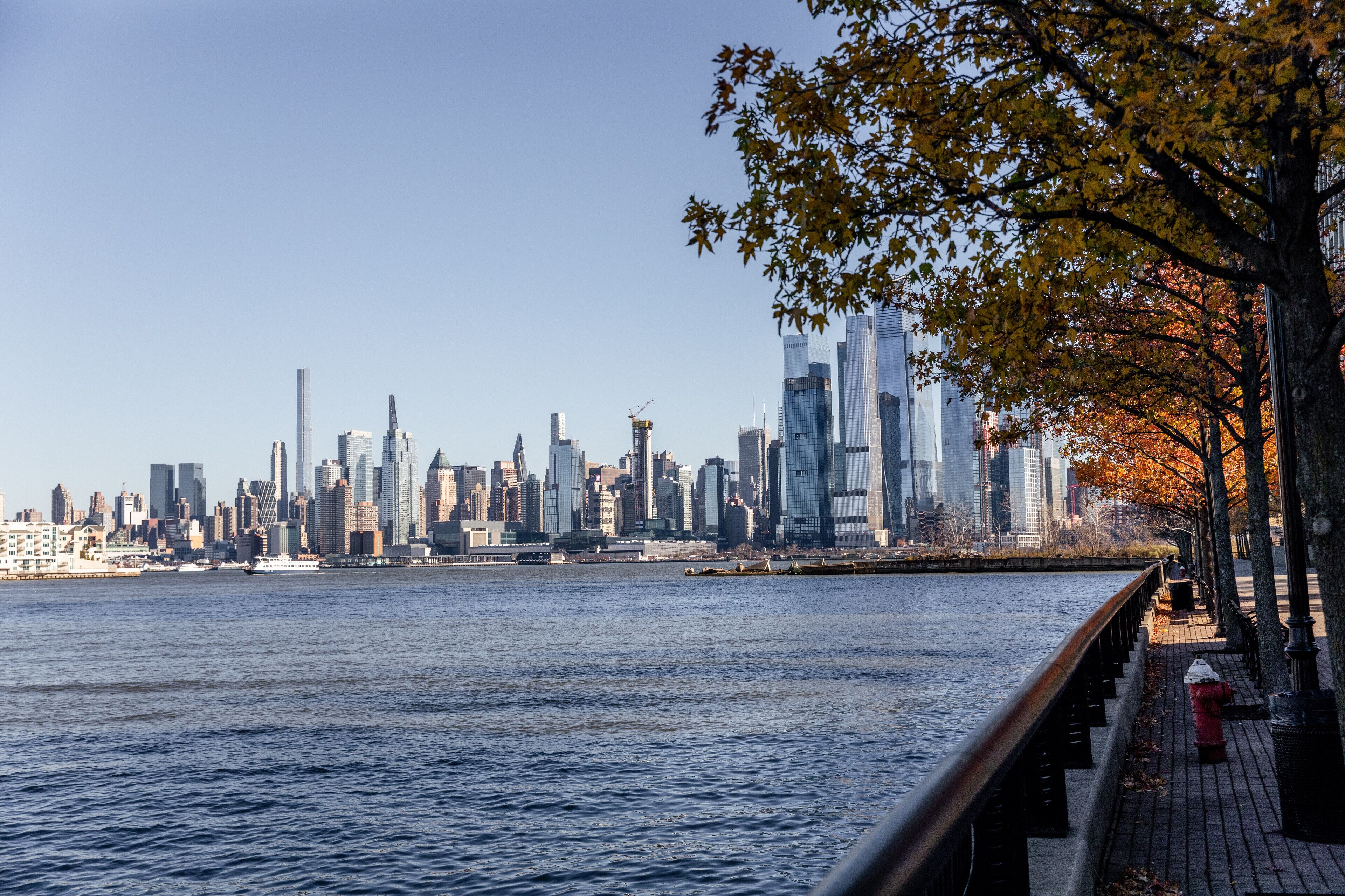 A waterfront cityscape with a prominent skyline of skyscrapers and a river.