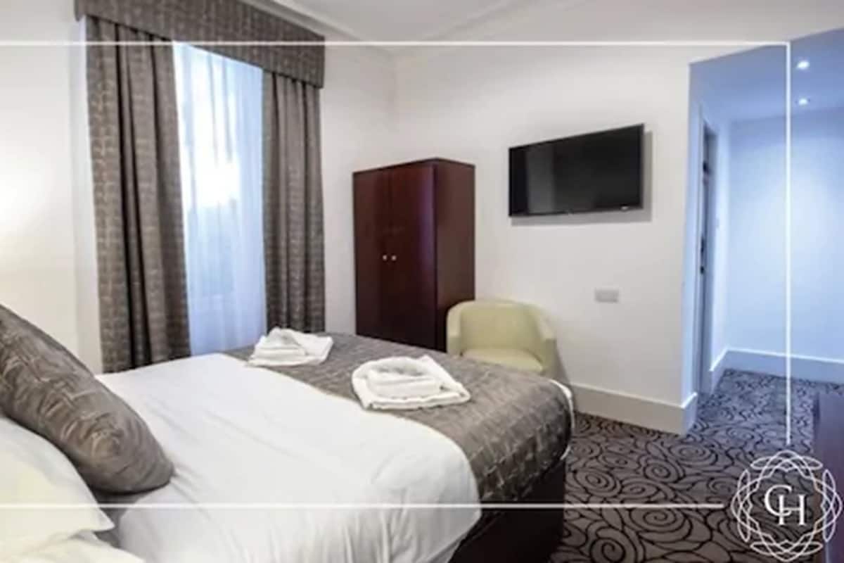 Quarto de hotel com cama, guarda-roupa, televisão e uma cadeira.