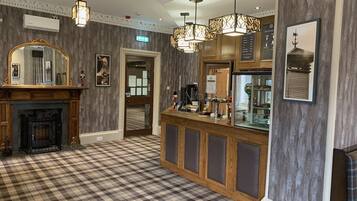 A hotel lobby with a checkered floor, a fireplace, a bar area with a beer tap, and a large mirror.