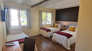 A hotel room with two beds, a wooden desk, a TV, and large windows with curtains. - Nova Posada (Colonia del Sacramento)