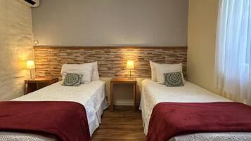 A room with two beds, wooden headboard, bedside lamps, and a window with curtains.