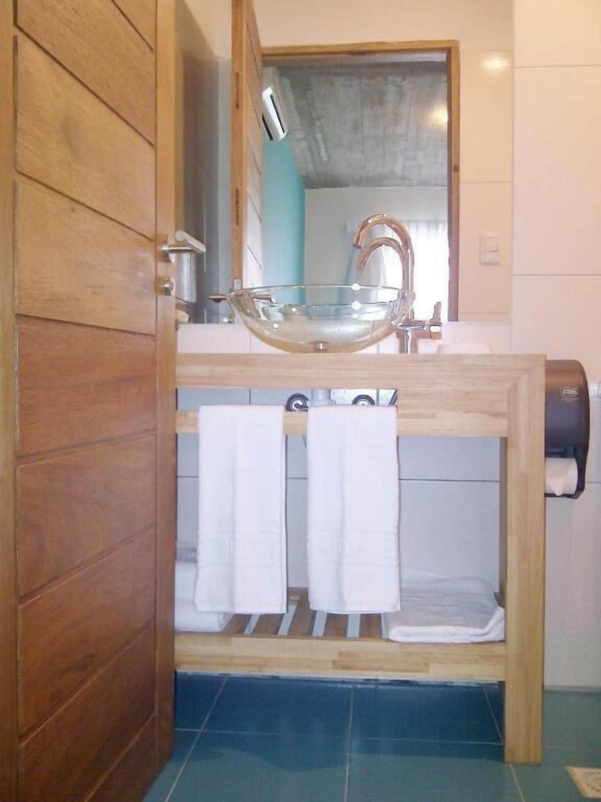 Un bagno con un mobile contenitore in legno, un lavabo in vetro e un porta asciugamani.
