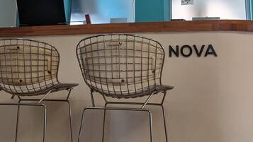 A reception area with a counter labeled "NOVA," two wireframe bar stools, a computer monitor, and a glass display case.