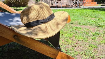 A straw hat on a wooden lounge chair in a garden area with outdoor furniture and a building in the background.