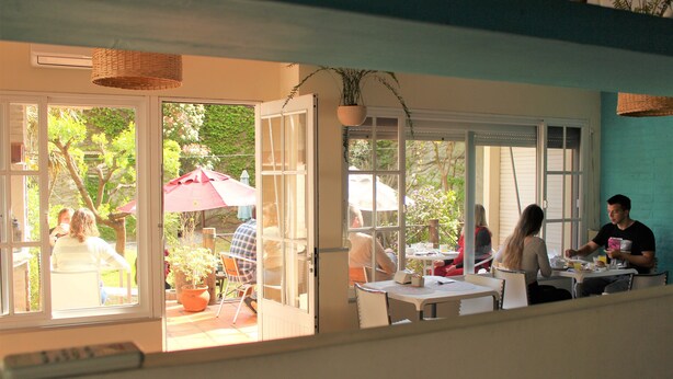 An open patio with tables and chairs, a potted plant, and a red umbrella. - Nova Posada (Colonia del Sacramento)