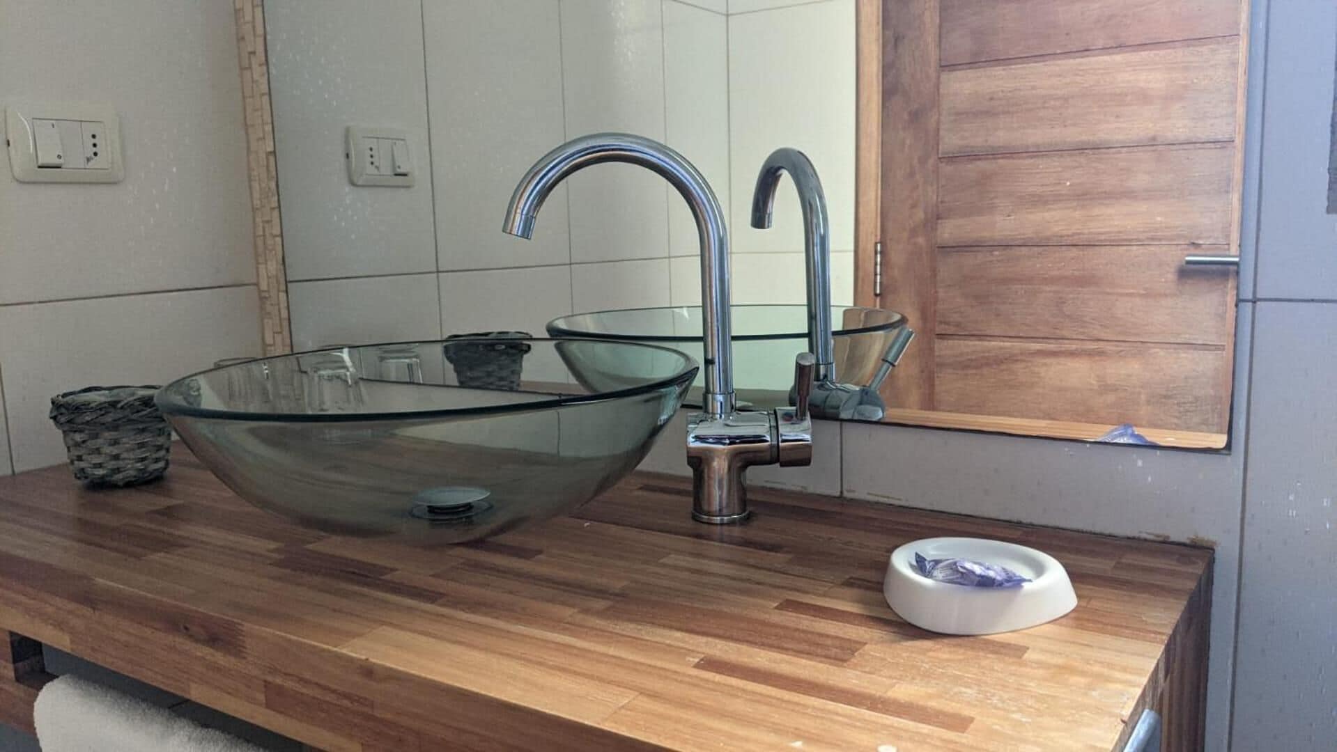 Een moderne badkamer met een houten wastafelmeubel, een glazen wastafel en een houten deur.