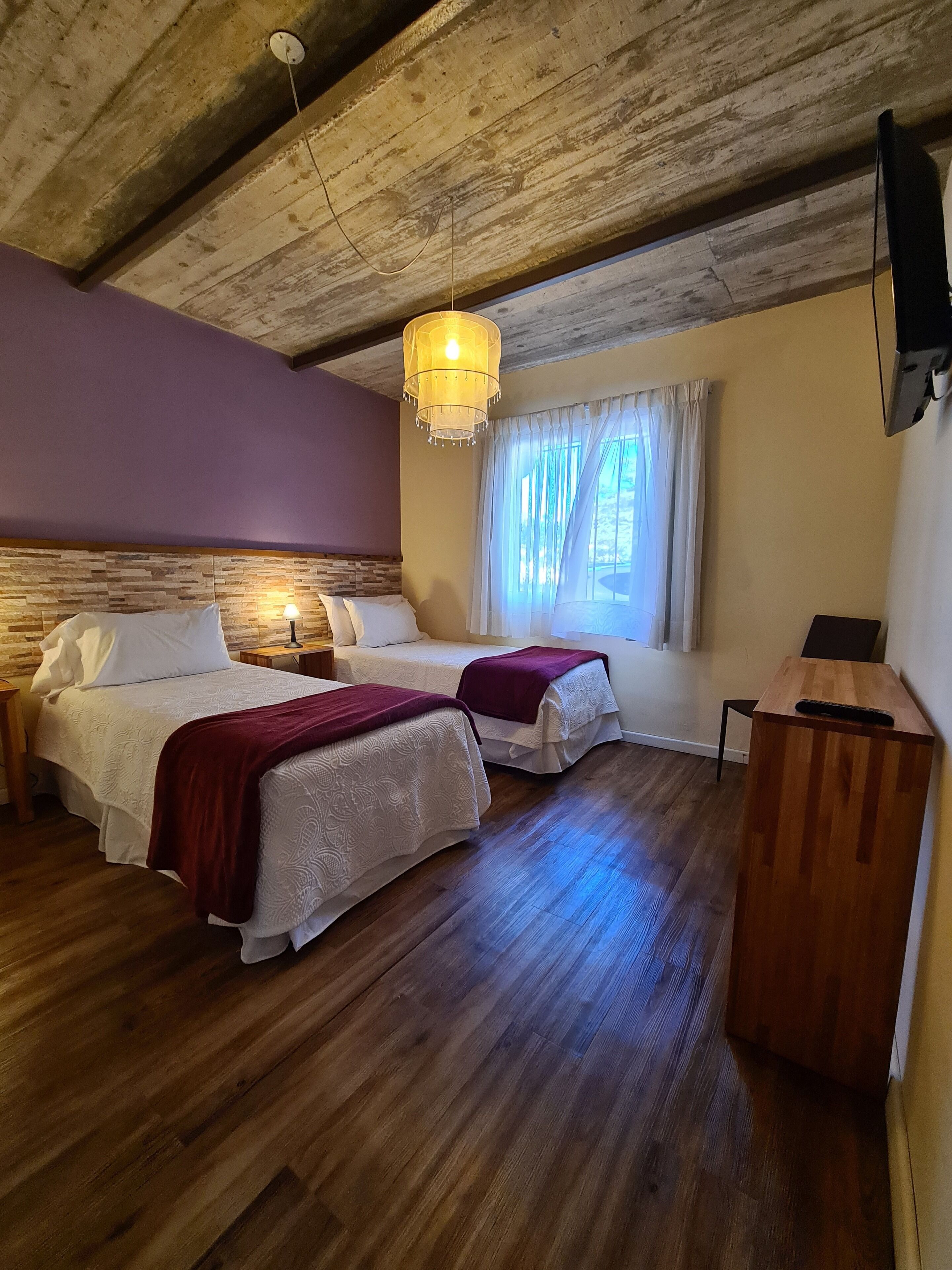 A room with two beds, a wooden desk, a television, and a window with curtains.