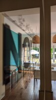 An interior space with a dining area featuring a table and chairs, a window with a view of the outdoors, and a hanging light fixture.