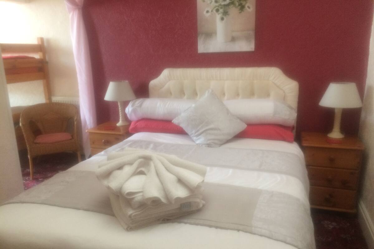 A neatly made bed with pillows and a folded blanket, a wooden chair, and two bedside tables with lamps.
