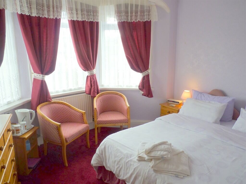 Habitación de hotel con una cama, dos sillas, una mesita de noche con lámpara y una ventana con cortinas.