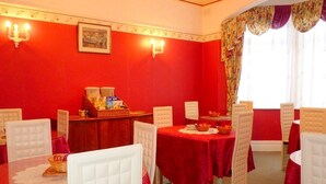 A dining room with red walls, white cushioned chairs, and tables set with red tablecloths. - Arendale Hotel (Blackpool)
