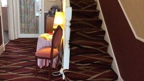 A carpeted staircase with a patterned carpet, a wooden chair with a cushion, a table with a lamp, and a door with a floral curtain. - Arendale Hotel (Blackpool)