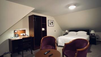Una habitación de hotel con cama, escritorio, silla, una mesita y un armario.