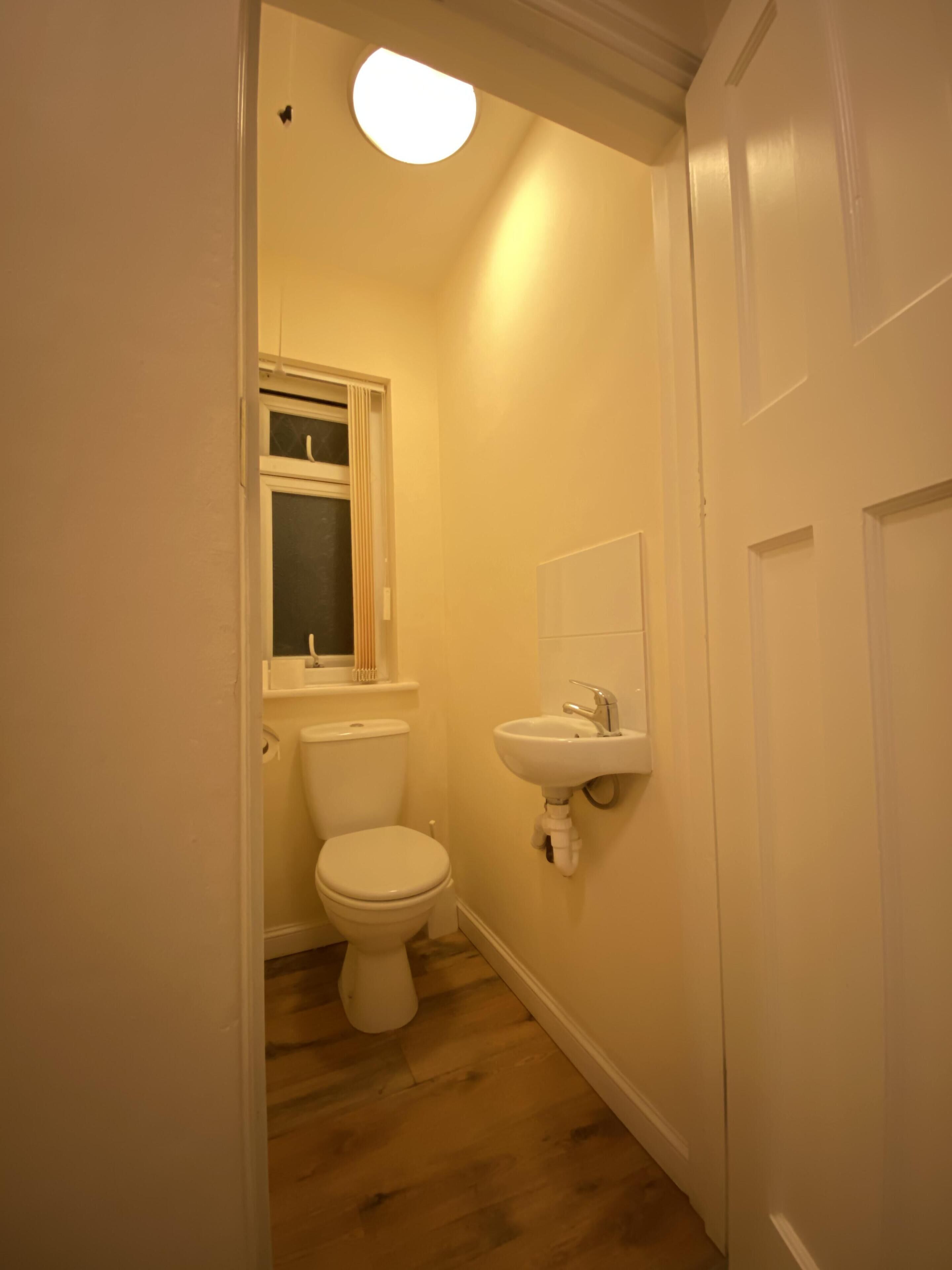Un baño pequeño y estrecho con inodoro, lavamanos y ventana sobre el inodoro.