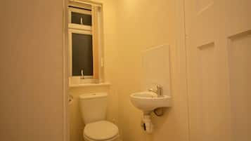Un baño pequeño y estrecho con inodoro, lavamanos y ventana sobre el inodoro.