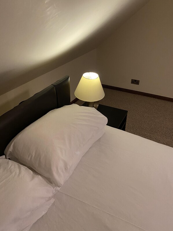 A hotel room with a bed, a nightstand, a lamp, and a power outlet on the wall. - Clifton House Brighton (Hove)