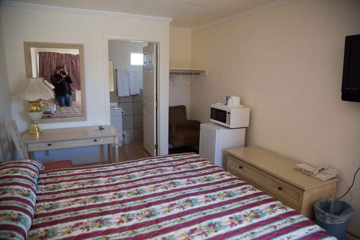 Un dormitorio con cama, escritorio, espejo, microondas y una cómoda pequeña.