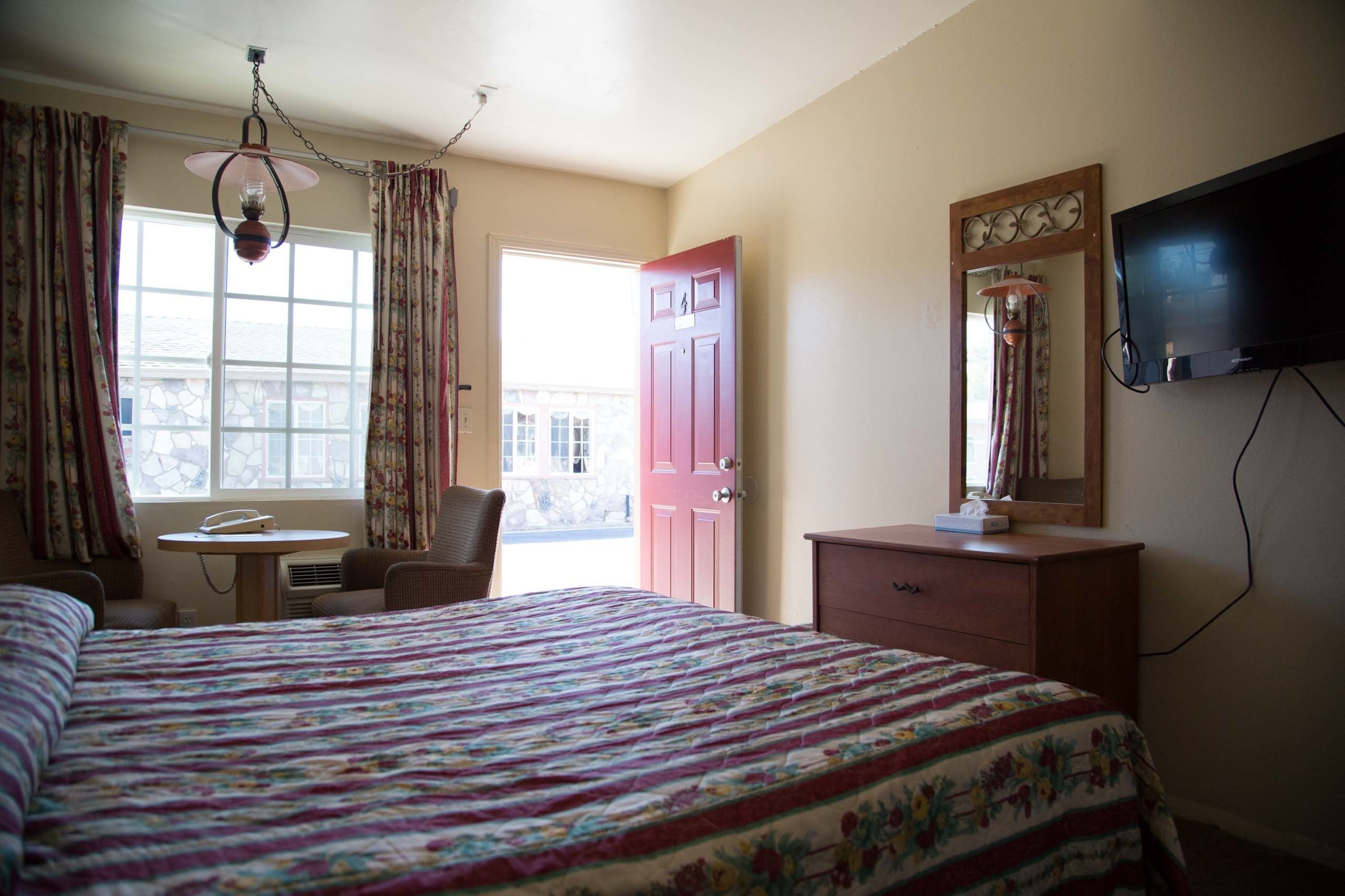 Quarto de hotel com uma cama grande, uma escrivaninha com cadeira, televisão e uma porta.