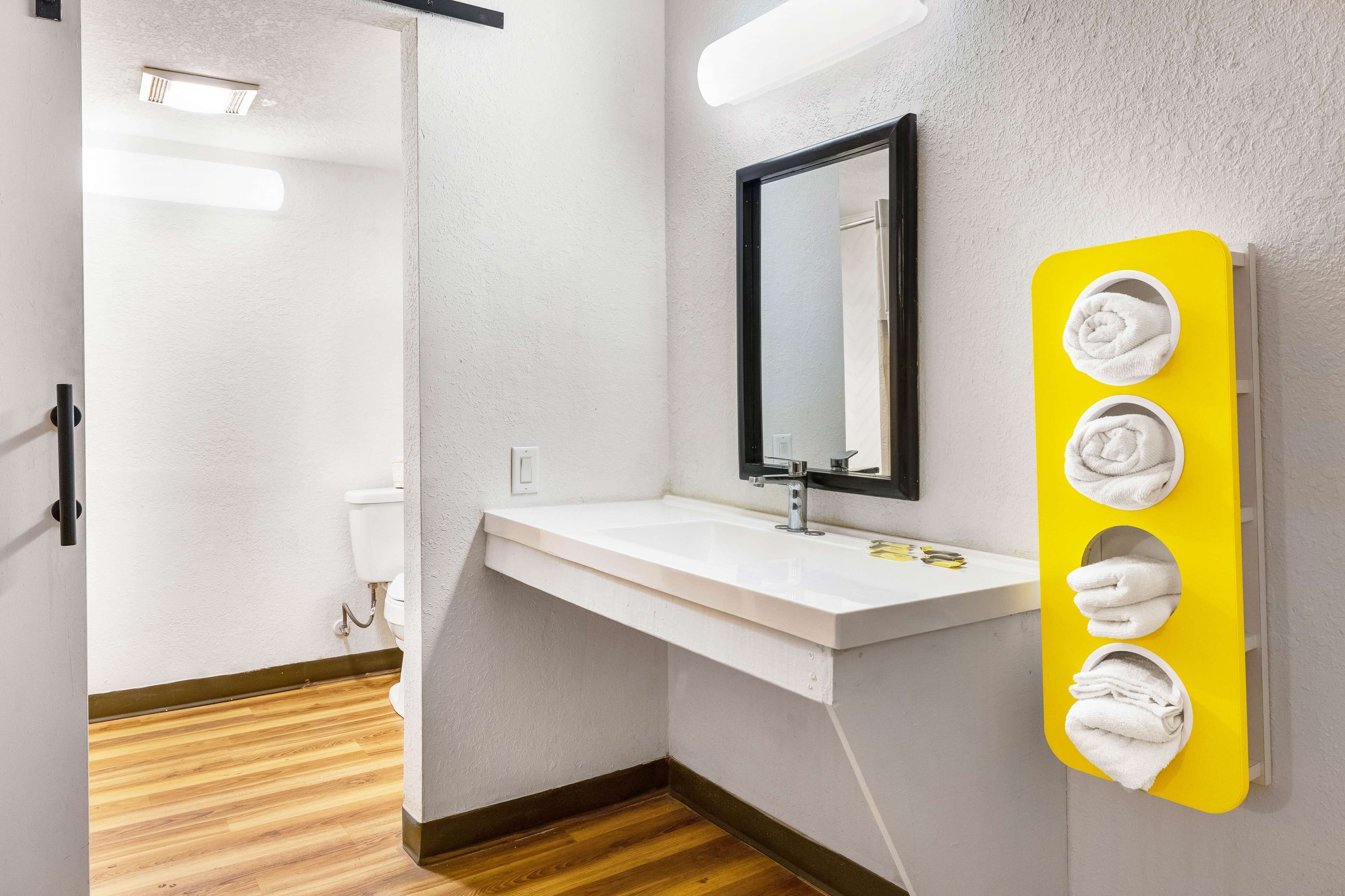 Un baño moderno con un lavamanos blanco, un espejo y un perchero amarillo.