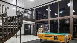 A pool table in a spacious indoor area with a spiral staircase and large windows. - Motel 6 Indianapolis, IN (Indianapolis)