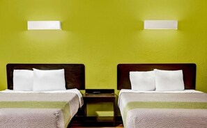 Ein Hotelzimmer mit zwei Betten, jeweils mit weißer Bettwäsche und Kissen, vor einer grünen Wand.