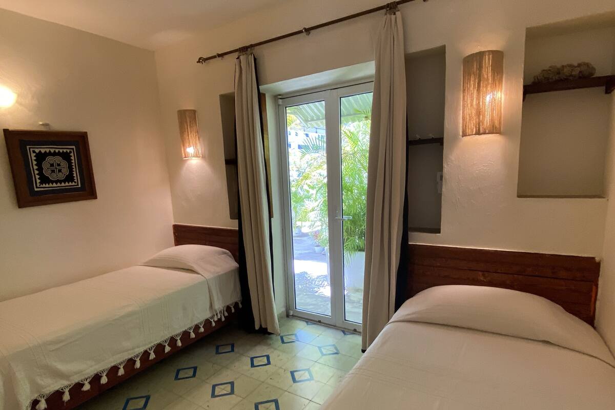 A hotel room with two single beds, a large sliding glass door leading to a balcony, a framed picture on the wall, and a tiled floor.