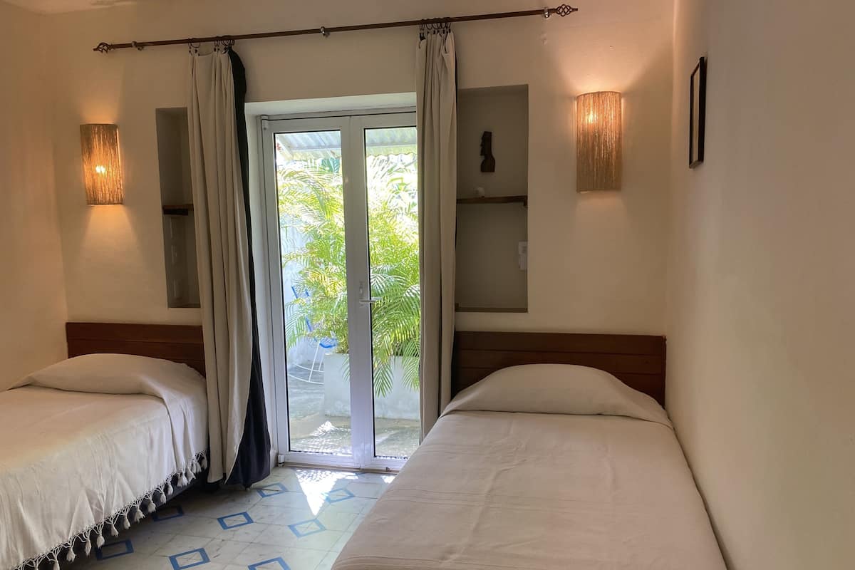 A room with two beds, a sliding glass door to a balcony, and a wall-mounted shelf with a decorative item.
