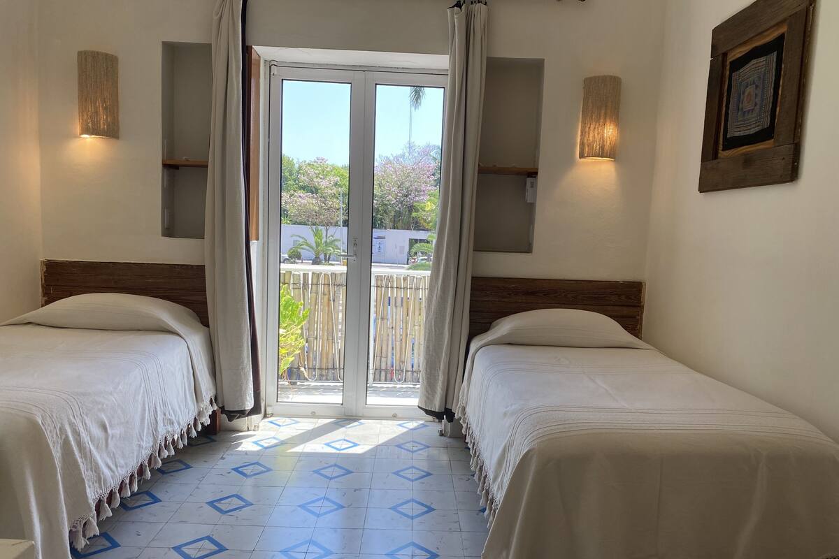 A room with two beds, a sliding glass door to a balcony, and patterned floor tiles.