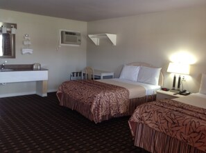 Ein Hotelzimmer mit Bett, Nachttisch, Lampe und einem Badezimmer mit Waschbecken und Spiegel.