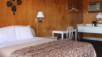 Ett hotellrum med en säng, ett skrivbord, en stol, en klädstång och ett badrum med en spegel och en handduksställning.