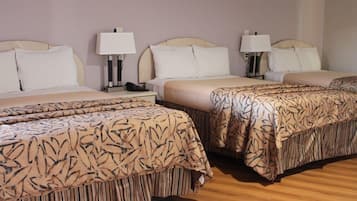 A hotel room with three beds, each with a patterned bedspread and white pillows. There are bedside lamps and a telephone on the nightstands.