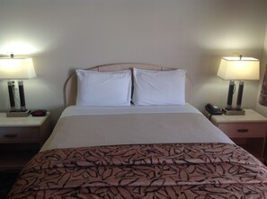 Ein Hotelzimmer mit einem Bett, zwei Nachttischen, zwei Lampen, einer Uhr und einem Telefon.