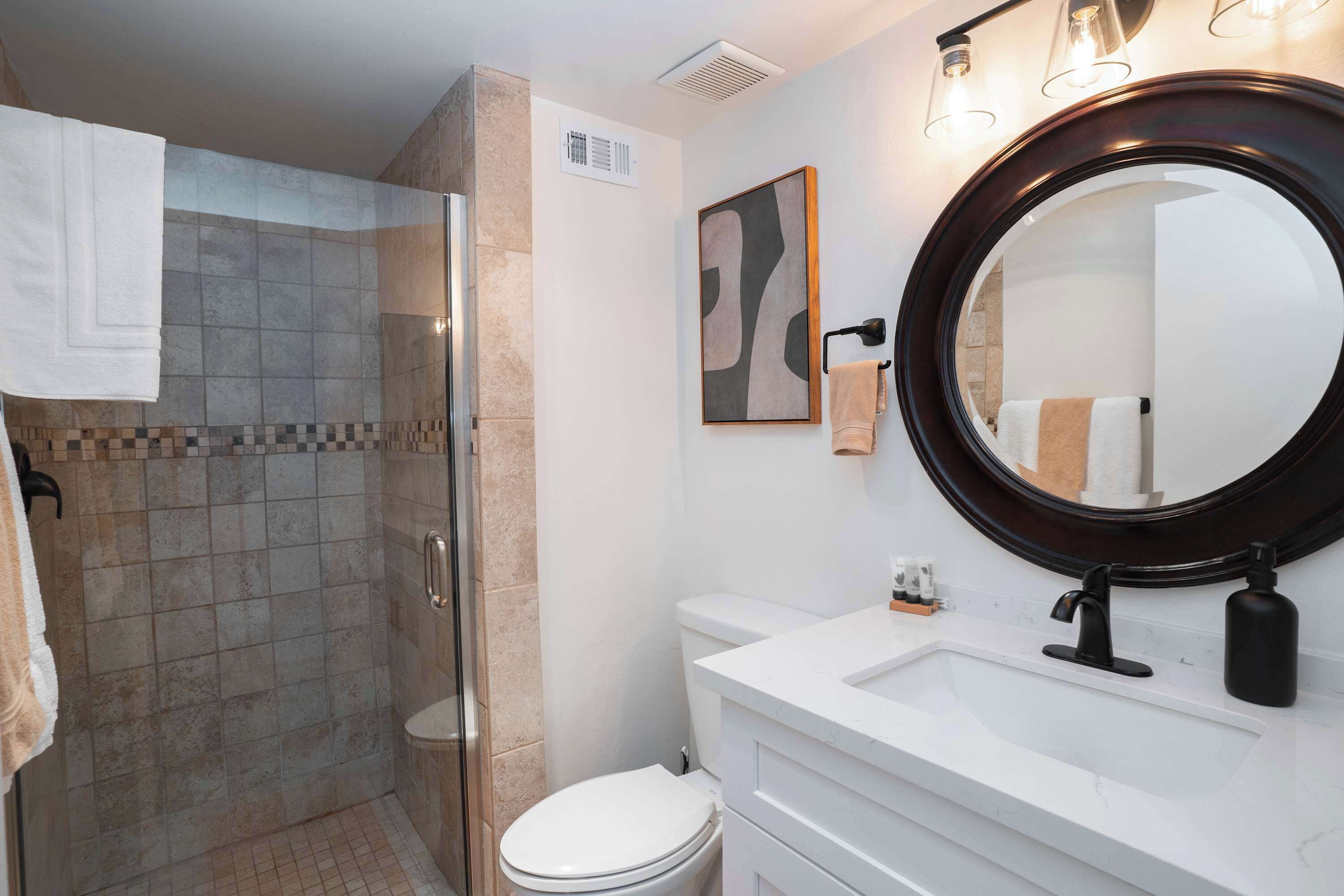 Un baño con ducha, inodoro, lavamanos y un espejo grande.
