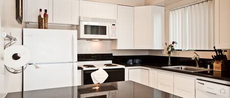 A modern kitchen with white cabinets, a black countertop, a built-in microwave, a stove, and a dishwasher.