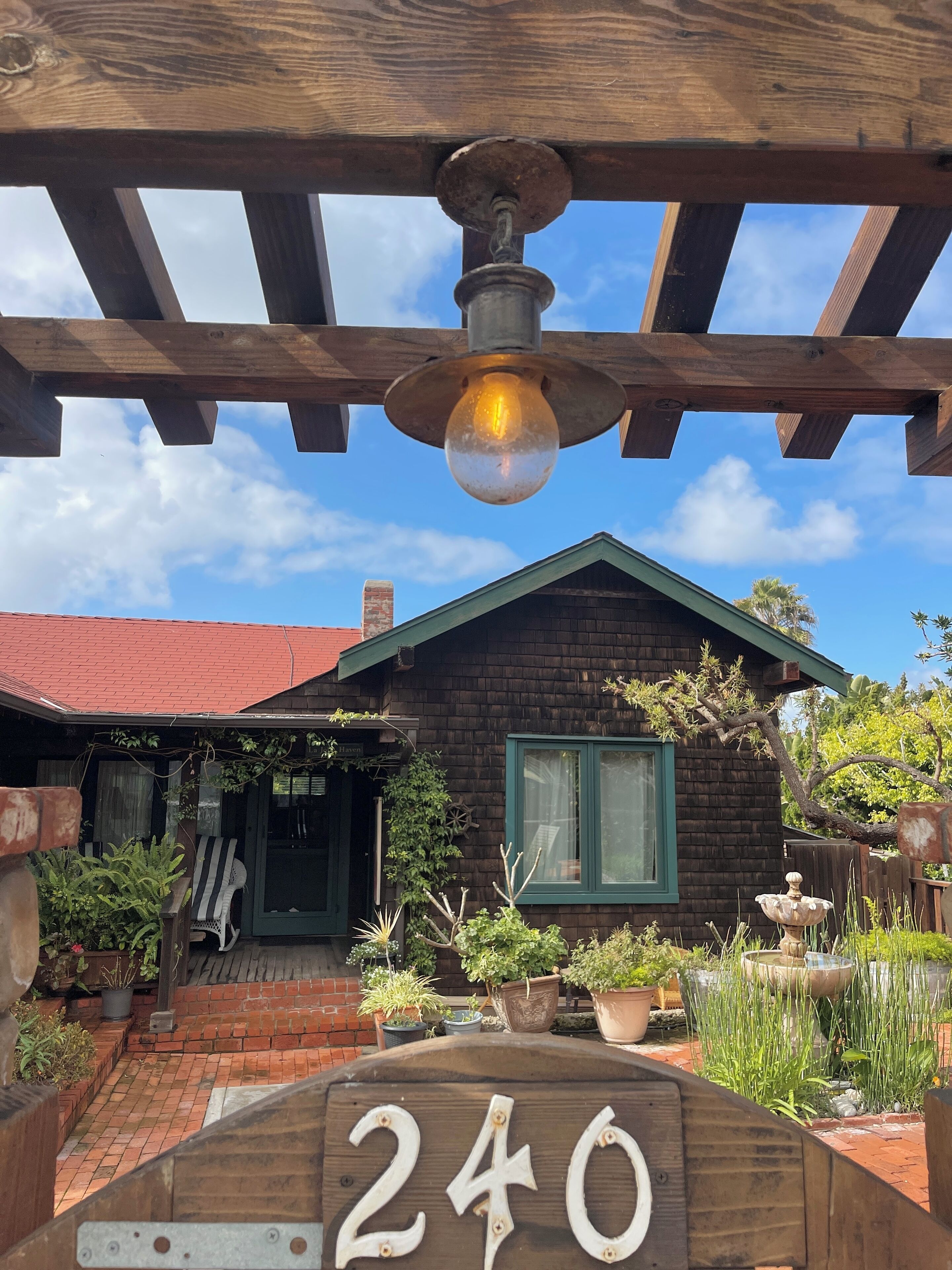 Uma casa de madeira com telhado verde, varanda com uma cadeira e placa com o número 240.